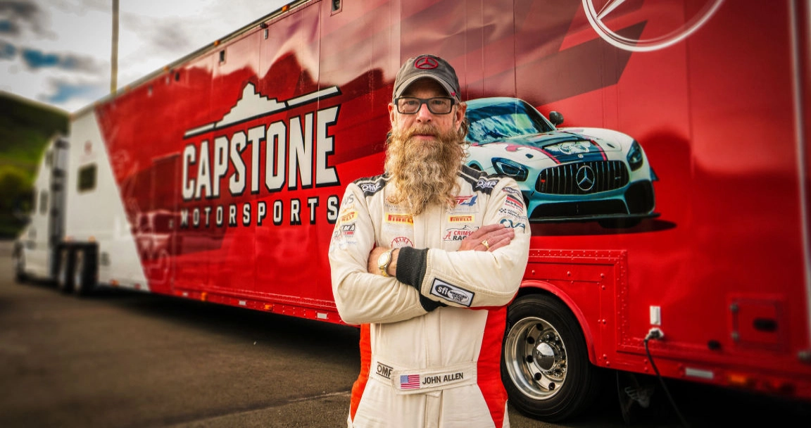 Man standing in front of racing trailer wrapped in red with vehicle on it