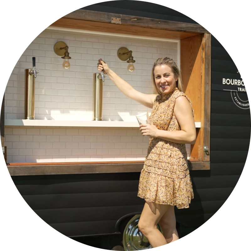 Jennifer standing at beverage trailer pouring beverage and smiling at camera