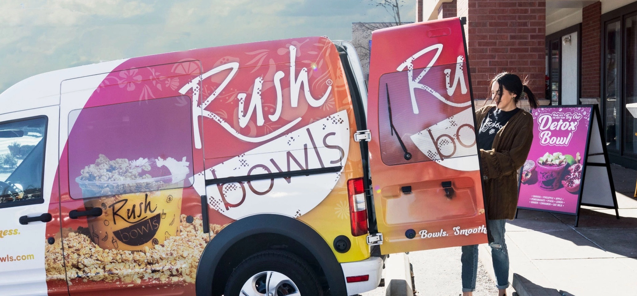 Women unloading van with brightly colored vehicle wrwap featuring granola and bowl.